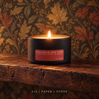 Lit Autumn in New York L+L candle in matte black travel tin against a warm maple-leaf patterned wall