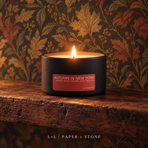 Lit Autumn in New York L+L candle in matte black travel tin against a warm maple-leaf patterned wall