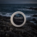Tōjinbō L+L candle silver lid with vetiver elemi and sea fragrance label photographed against dark ocean waves